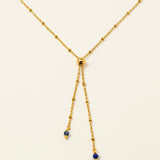 Collier Essaouira, chaîne satellite dorée forme Y et perles lapis-lazuli, fond crème